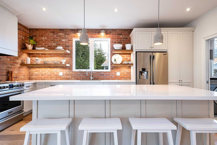 A kitchen with a brick wall, and white countertops with a kitchen island and chairs in Wasaga beach Ontario.